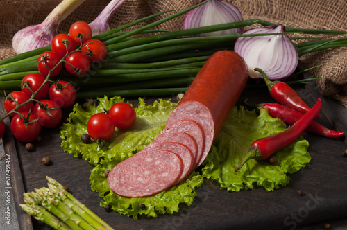 smoked servelat on a wooden board decorated with fresh vegetables photo