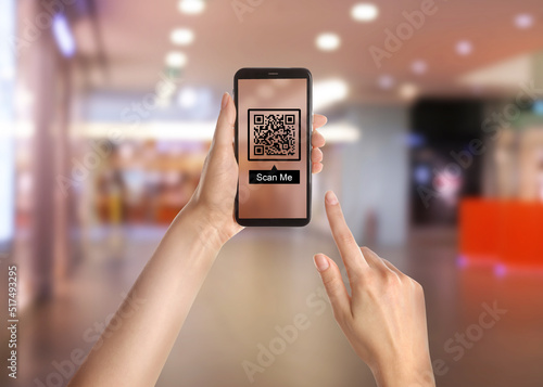 Woman holding smartphone with QR code on screen in shopping mall, closeup