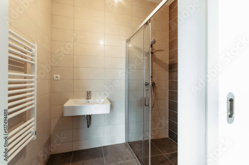 A small simple bathroom without a mirror.  The bathroom has a large rectangular sink  a large and spacious shower with sliding glass doors and a heating ladder.
