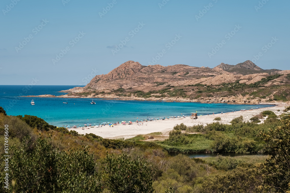 Holidaymakers enjoying the sunshine and turquoise Mediterranean sea in the Balagne region of Corsica with the rocky coast of Desert des Agriates behind
