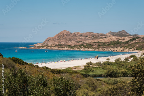 Holidaymakers enjoying the sunshine and turquoise Mediterranean sea in the Balagne region of Corsica with the rocky coast of Desert des Agriates behind