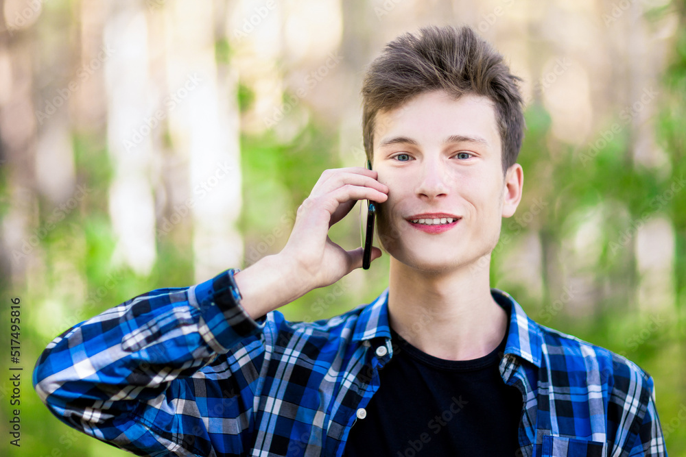 Happy smiling teenage boy talking on a smart phone in a summer forest. Happy smiling teenage boy talking on a smart phone in a summer forest.