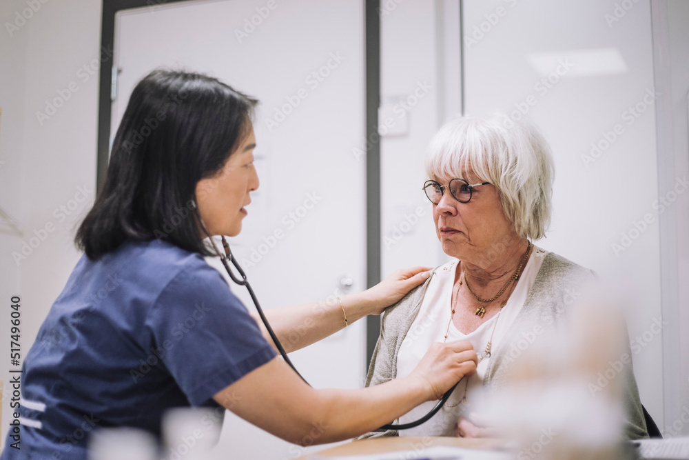 Female healthcare worker examining senior patient with stethoscope in medical clinic Female healthcare worker examining senior patient with stethoscope in medical clinic