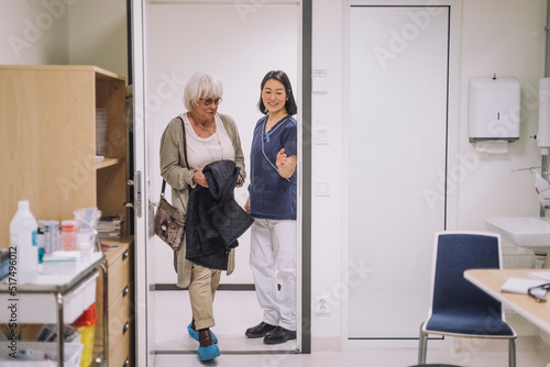 Smiling doctor gesturing to senior patient entering office at hospital photo