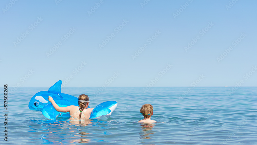 Kids are playing the sea. Little baby boys and girl in goggles with inflatable toy float shark and dolphin playing in the water on summer vacation. Babyproof on the beach and sea