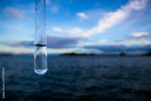 Water sample. Test tube with water. Sea and blue sky in the background. Water purity analysis and environment concept. Water testing. Infections and bacteria.