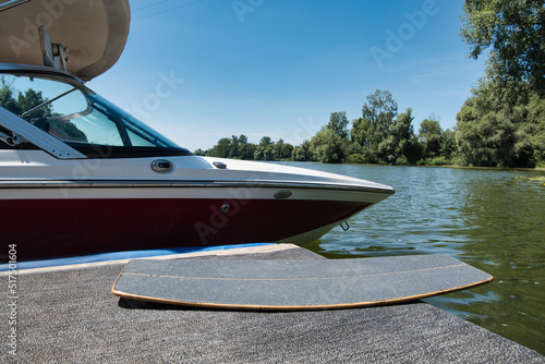Wakeskate board lying next to a ski boat, wakeboard boat which is docked at the pier. A calm and empty lake in the background. Adventure, leisure, action sports scene.  © Philipp