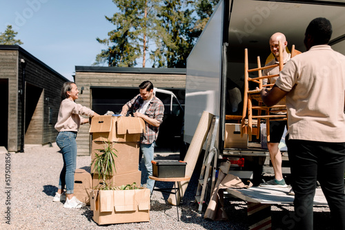 Professional movers carrying chairs from truck while couple looking through boxes photo
