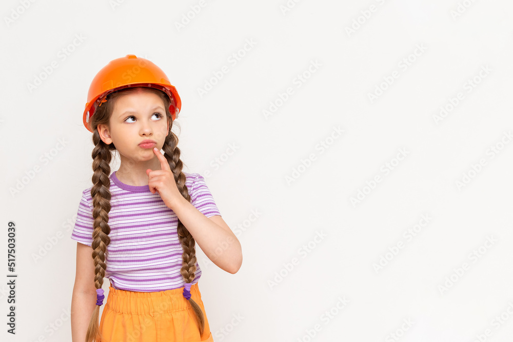 A little girl in a construction helmet looks at your advertisement on a white isolated background. Copy space. The concept of renovation in the children's room. A little girl in a construction helmet looks at your advertisement on a white isolated background. Copy space. The concept of renovation in the children's room.