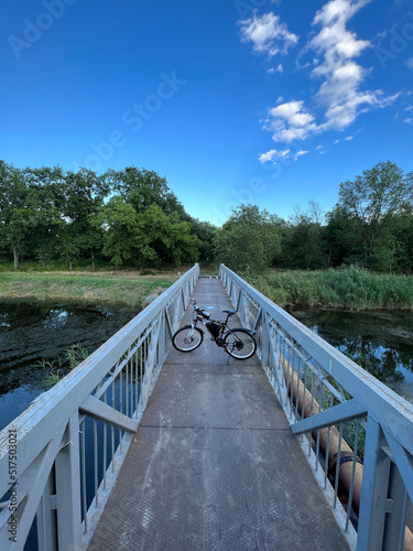 Canvastavla Electric bicycle stands among narrow footbridge through river.