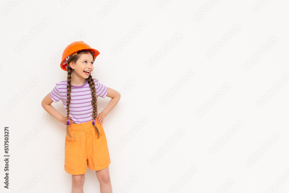 A little girl in a construction helmet looks at your advertisement on a white isolated background. Copy space. The concept of renovation in the children's room. A little girl in a construction helmet looks at your advertisement on a white isolated background. Copy space. The concept of renovation in the children's room.