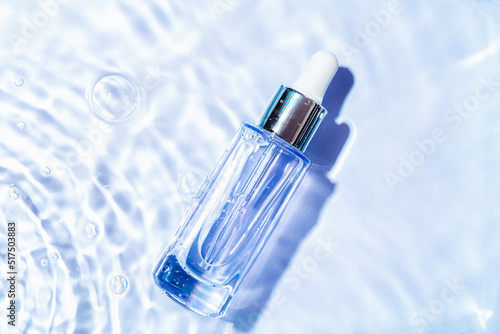 Glass serum bottle with collagen on blue water background with water bubbles. Advertising of medical product for anti-aging care. Cosmetic spa medical skincare. Top view