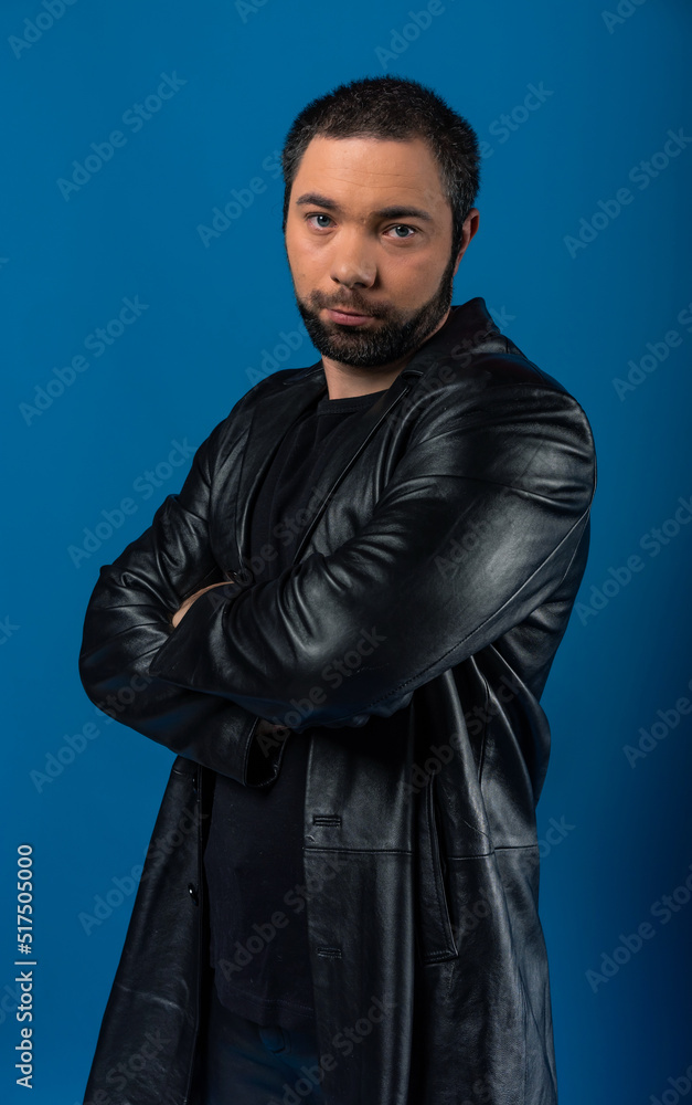 portrait of a man in a studio in a black leather coat. model with a beard on a blue background. portrait of a man in a studio in a black leather coat. model with a beard on a blue background.