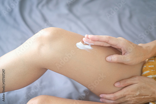 Asia woman sitting on bed and applying cream on her leg. © BoszyArtis
