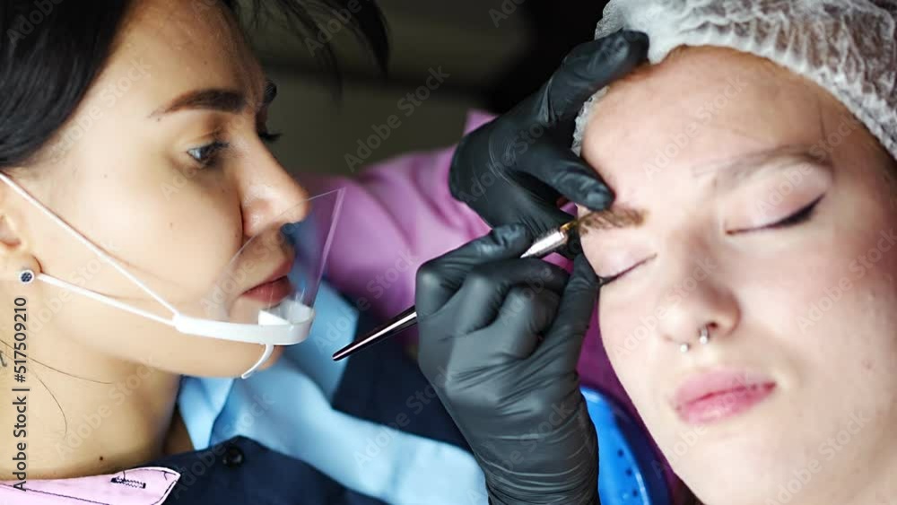Procedure of eyebrow microblading. A master in black gloves is doing a blending needle of model's brow. Procedure of eyebrow microblading. A master in black gloves is doing a blending needle of model's brow.