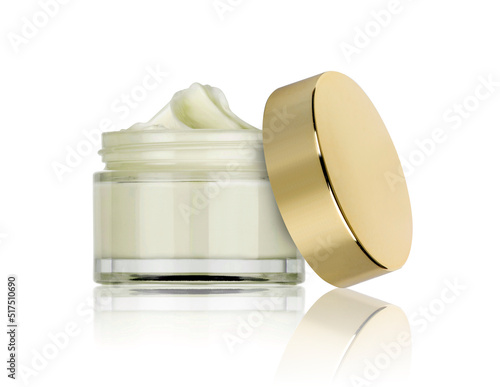 glass jar of beauty cream with golden lid resting on the side and reflected in the white plane
