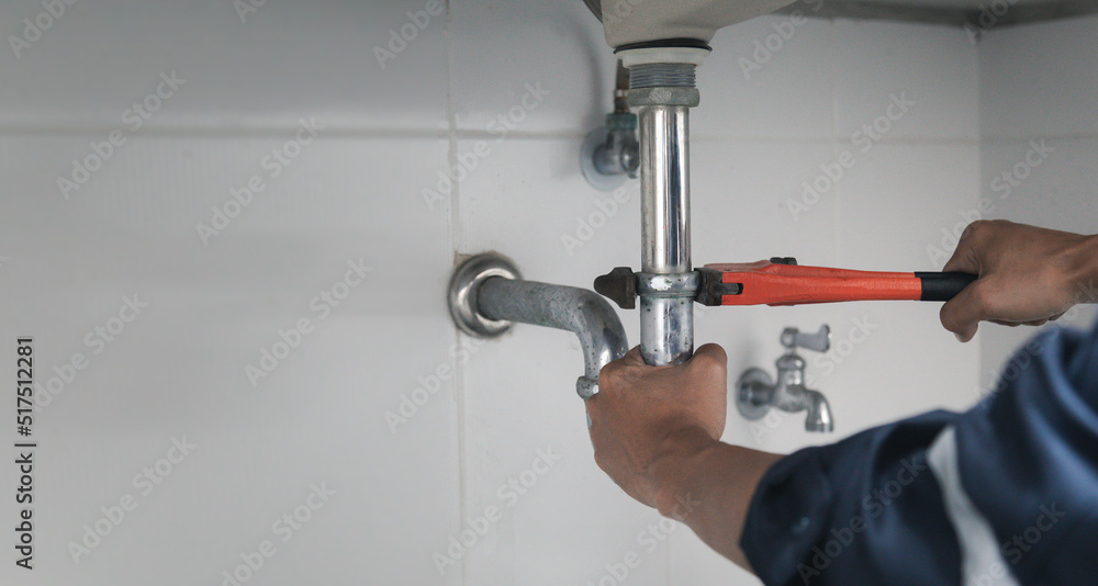 Male Plumber Using Wrench To Fix Leaking Sink In Home Bathroom. Male Plumber Using Wrench To Fix Leaking Sink In Home Bathroom.