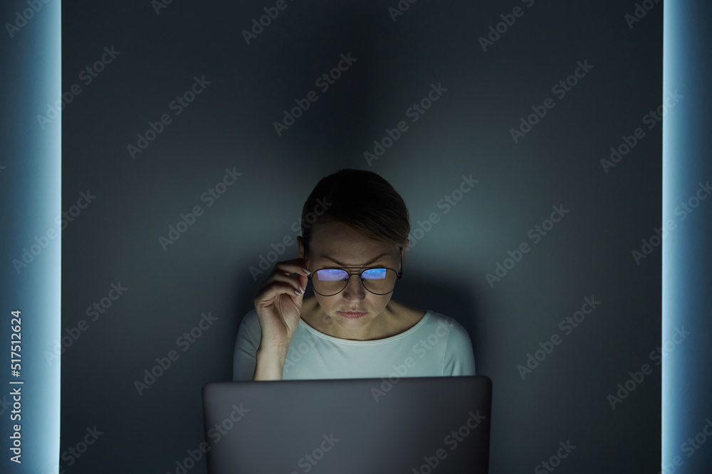 Confident young woman working on laptop against a dark wall