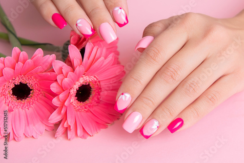 Beautiful female hands with romantic manicure nails, pink gel polish, gerbera flowers design