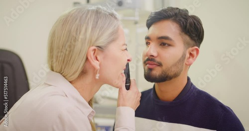 Wallpaper Mural Optometrist doing an eye test on a patient in a clinic. Female optician assessing the vision of a young man with a retinoscope. Eye care professional helping to correct sight with prescription lenses Torontodigital.ca