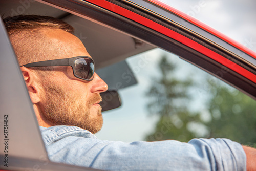 A man with a smile on his face drives a red car.