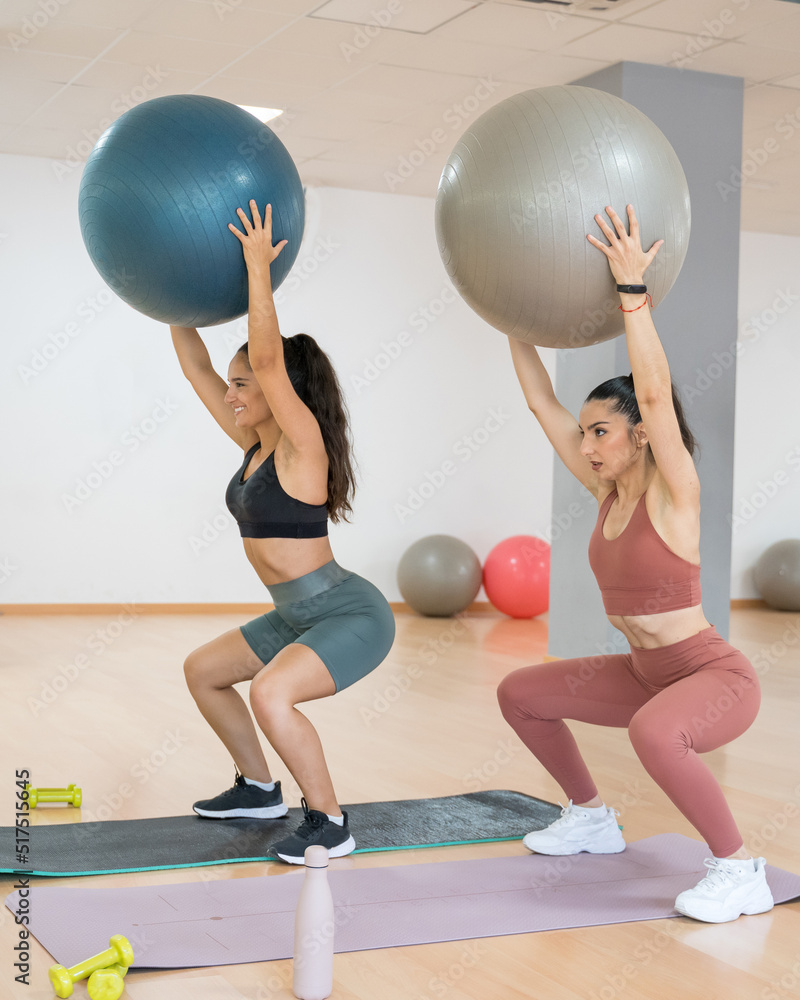 Fototapeta premium TWO GIRLS TRAINING YOGA AND PILATES TOGETHER WITH A BALL AND WEIGHTS