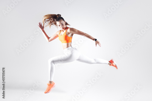 Beautiful young woman in sports clothing running against white background