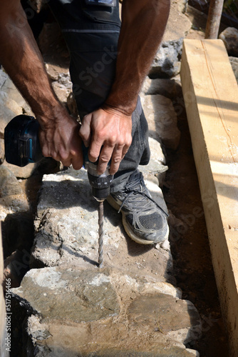 Worker of construction drilling stone with a power drill. Making a hole in the foundation of a house using a perforator with a long drill