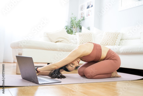 YOUNG GIRL DOING YOGA AND PILATES IN THE LIVING ROOM OF HER HOME WITH THE COMPUTER
