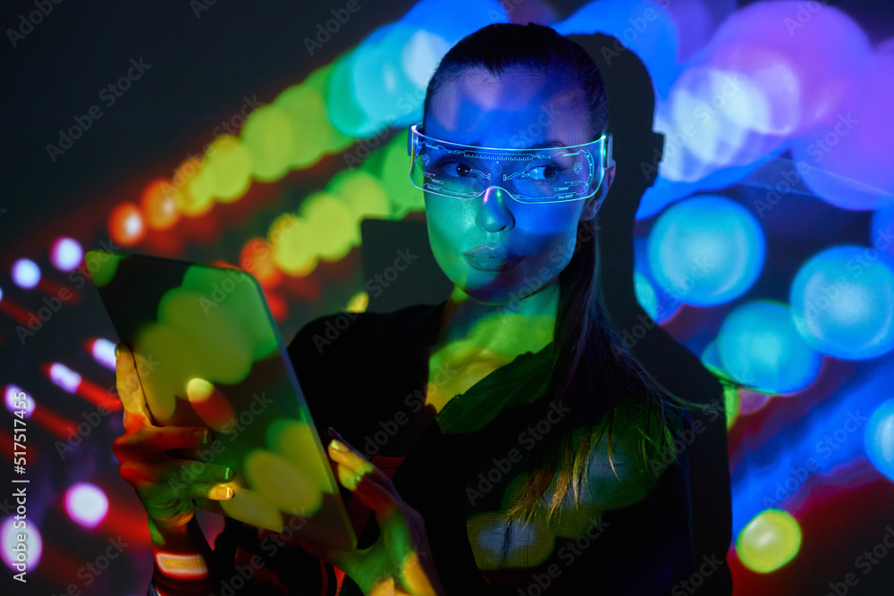 Beautiful young woman in futuristic glasses using digital tablet against colorful background