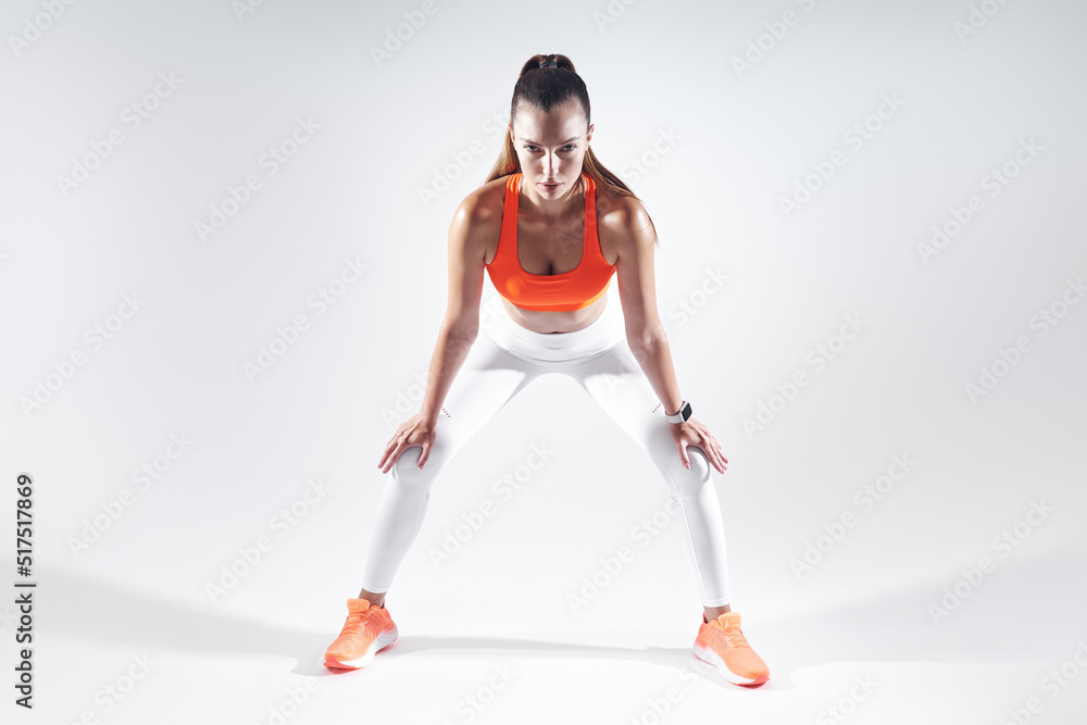 Beautiful young woman leaning on knees while standing against white background Beautiful young woman leaning on knees while standing against white background