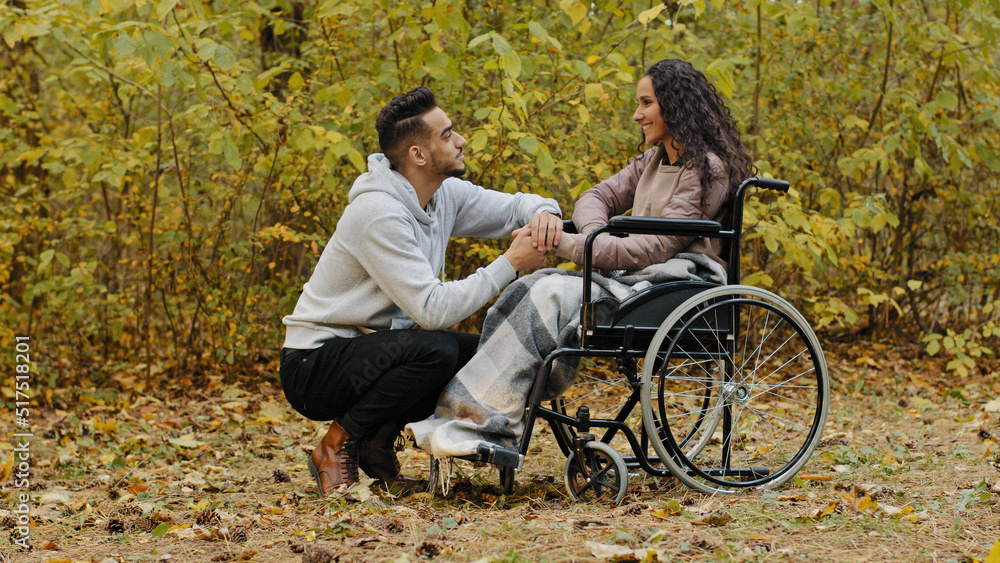 Young happy hispanic couple in love having cute conversation talking caring boyfriend visits sick girlfriend in hospital park woman patient in wheelchair needs rehabilitation loving guy supports girl Young happy hispanic couple in love having cute conversation talking caring boyfriend visits sick girlfriend in hospital park woman patient in wheelchair needs rehabilitation loving guy supports girl