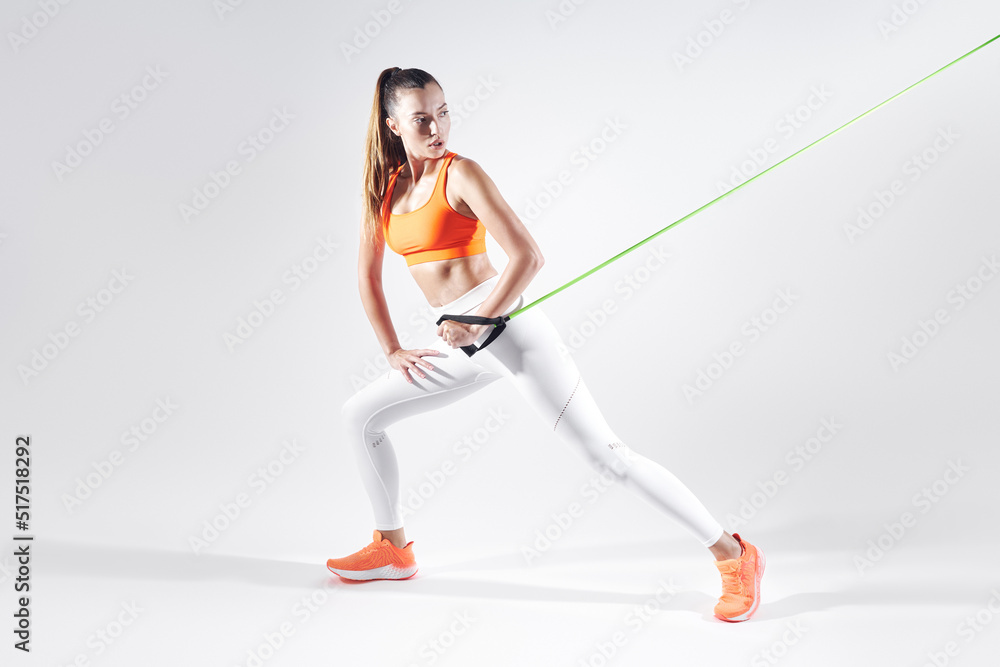 Beautiful woman in sports clothing using resistance band while exercising against white background Beautiful woman in sports clothing using resistance band while exercising against white background