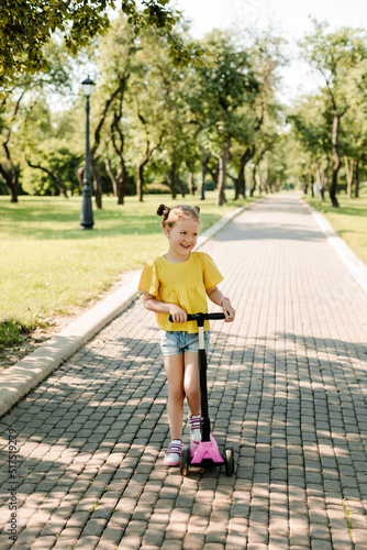 An active little girl rides a scooter on a path in an outdoor park on a summer day. Seasonal children's active sport. Healthy lifestyle in childhood