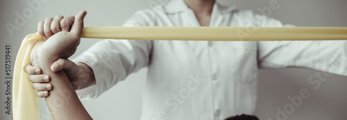 Physical therapy, Female physiotherapist uses an elastic band to test the arm injury of a male patient attending in clinic, Bone arrangement, Non-surgical medical treatment, Medical techniques.