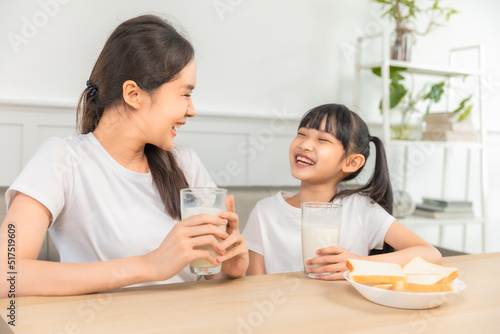 Asian family enjoying breakfast at living room. little girl daughter sitting on table, drinking milk with smiling father and mother in morning. Happy family at home.