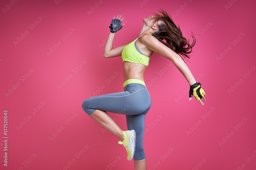 Confident young woman in sports clothing exercising against pink background