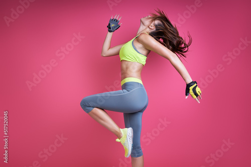 Confident young woman in sports clothing exercising against pink background