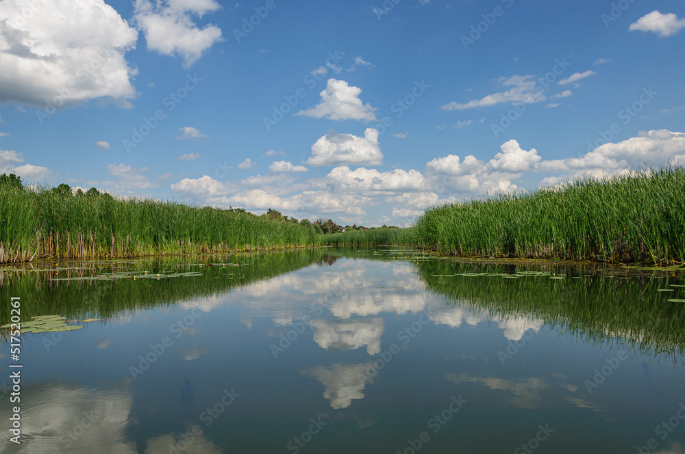 A beautiful sky with white clouds is reflected in the calm water of the Zdvizh River. Ukraine