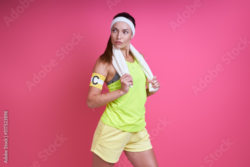 Confident woman in sports clothing carrying towel on shoulders against pink background
