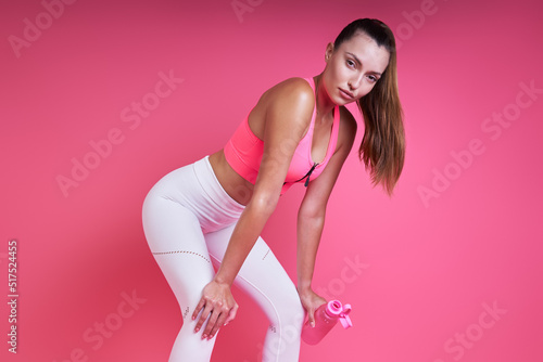Fototapeta Naklejka Na Ścianę i Meble -  Relaxed young woman leaning on knees while standing against pink background