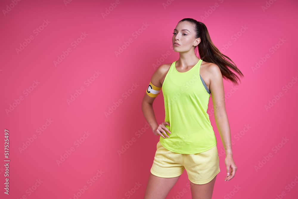 Beautiful woman in sports clothing wearing captain band and standing against pink background Beautiful woman in sports clothing wearing captain band and standing against pink background
