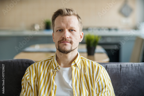Head and shoulders portrait of serious unshaved middle aged man with blue eyes looking at camera at home