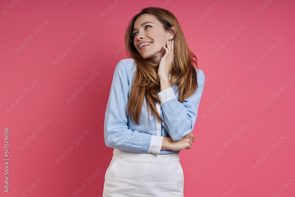Dreamful young woman looking away while standing against colored background Dreamful young woman looking away while standing against colored background