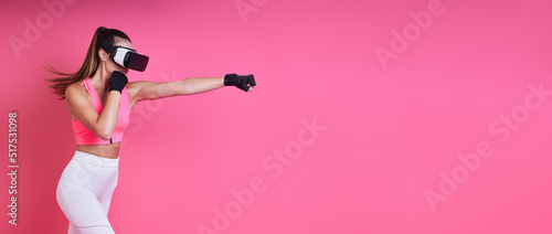 Confident young woman in virtual reality glasses boxing against pink background