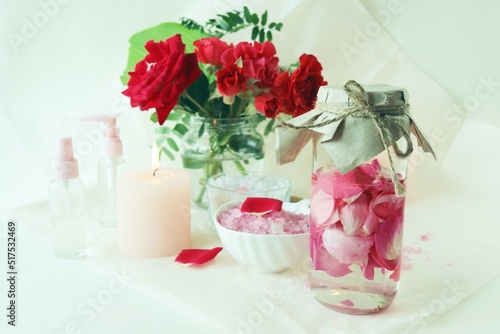 Bouquet of fresh red roses, water with pink rose petals, sea salt and burning candles, on a light background, natural cosmetics, body care, emotion of love