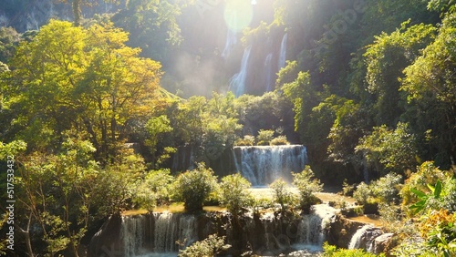 Beautiful waterfall in green tropical forest. Mountain jungle with limestone waterfalls cascades. Powerful raging whitewater falling stream. Slow motion. Lens flare, shining sun, hot summer day. © TravelMedia