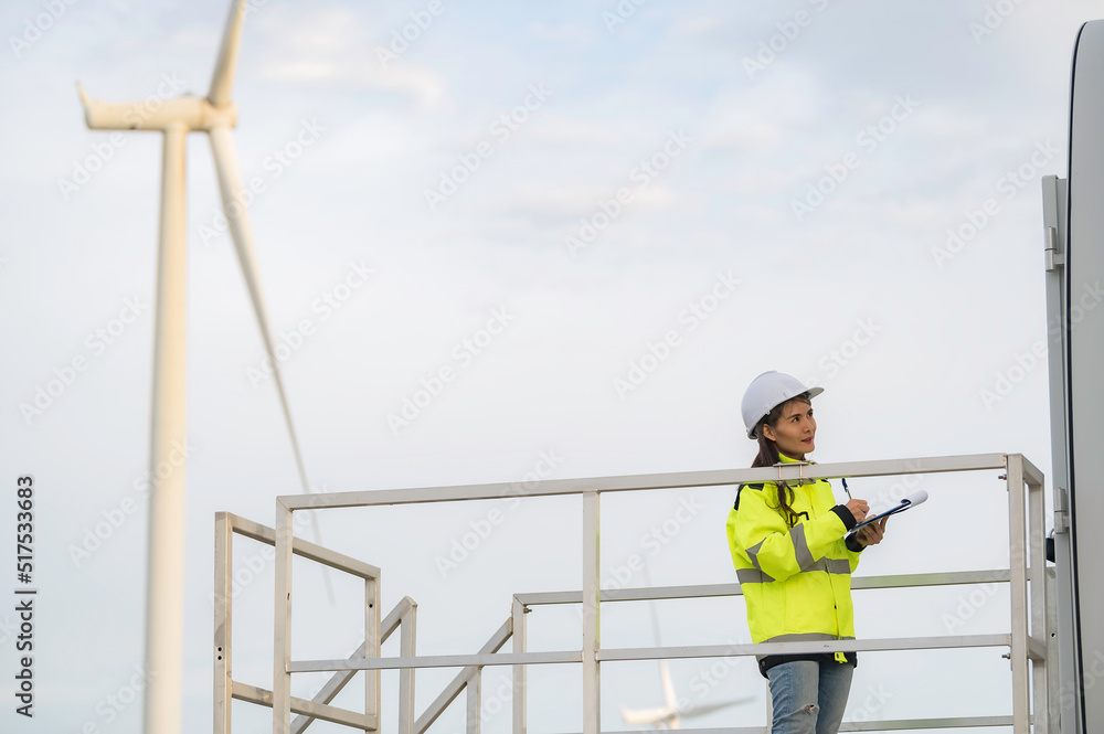 women engineer working and holding the report at wind turbine farm Power Generator Station on mountain,Thailand people women engineer working and holding the report at wind turbine farm Power Generator Station on mountain,Thailand people