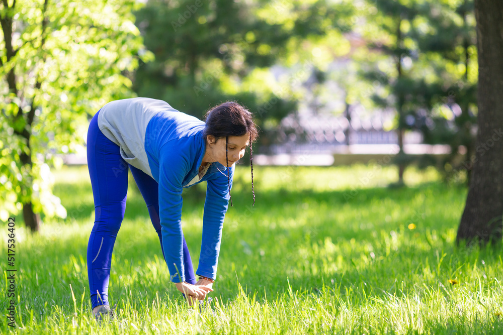 35-year-old woman is warming up in city park. She stretching and warming up the muscles of the legs. 35-year-old woman is warming up in city park. She stretching and warming up the muscles of the legs.
