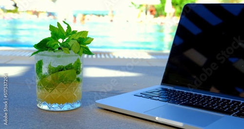 A photo of a laptop and a cocktail on the poolside